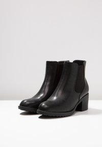 Botas negras hasta el tobillo hechas de cuero brillante con paneles laterales elásticos y un tacón robusto. Suela de goma texturizada para mayor agarre.