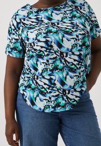 Haut multicolore à manches courtes avec des motifs abstraits bleus, verts et noirs. Encolure ronde et coupe fluide, fabriqué en tissu léger et texturé.