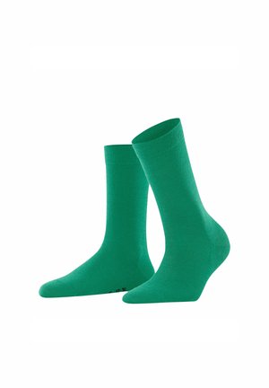 Ein Paar schlichte grüne Socken in Crew-Länge, eine aufrecht und eine leicht geneigt, vor einem weißen Hintergrund präsentiert.