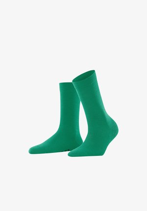 Ein Paar schlichte grüne Socken in Crew-Länge, eine aufrecht und eine leicht geneigt, vor einem weißen Hintergrund präsentiert.