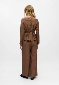 Brown, long-sleeve, belted jumpsuit with a peplum waist and wide-leg pants. Smooth fabric with a subtle sheen. Keyhole back detail.