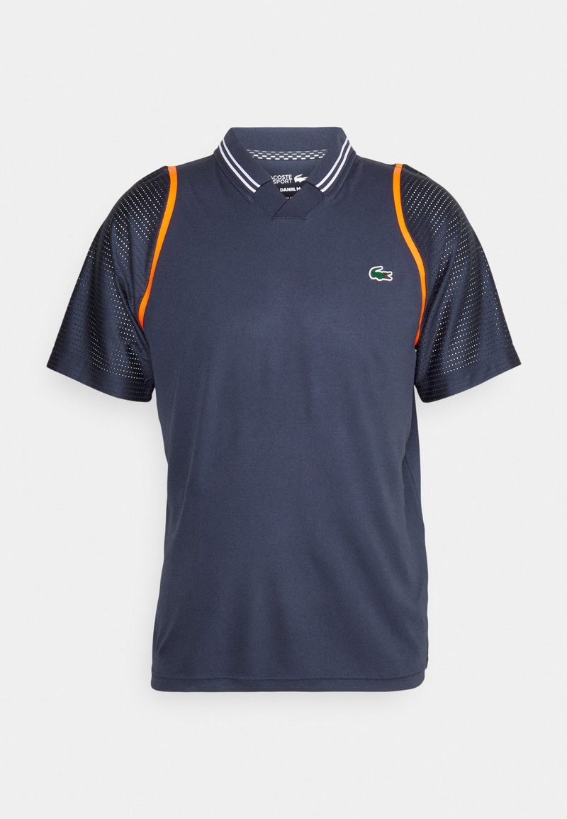 Polo de sport marine à manches courtes, doté de panneaux latéraux en maille, d'un col rayé blanc et d'un accent orange sur l'épaule. Logo Lacoste sur la poitrine.