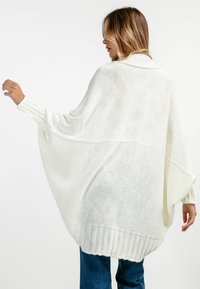 Biały, dziergany, oversize sweter z wysokim kołnierzem, szerokimi rękawami i prążkowanym wykończeniem. Lekki, o luźnej, przewiewnej strukturze.