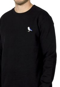 Sort sweatshirt med et lille, broderet fugledesign i hvidt og blåt på venstre brystområde. Blødt stofmateriale med rund hals.