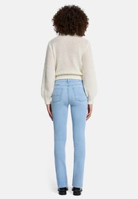 Kremowy sweter dziany z cropped designem i prążkowanym wykończeniem, zestawiony z jasnoniebieskimi dopasowanymi dżinsami. Czarne obuwie dopełnia całość.