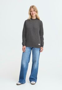 Grå sweatshirt med høy hals, lange ermer, ribbede mansjetter og nederkant, kombinert med vide blå jeans og grå joggesko.