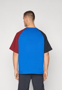 Blue, red, and black color-blocked short-sleeve t-shirt with a rounded neckline and a subtle v-shaped seam detail on the back.