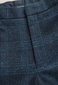 Tela de color azul oscuro con una textura y un patrón sutilmente tejido. Presenta una cintura lisa y una línea de pliegue limpia a lo largo del frente.