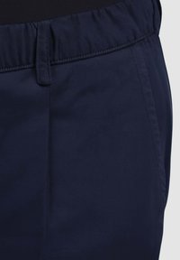 Pantaloni blu navy con una cintura elastica e una texture liscia. Presentano una parte anteriore piatta e una tasca laterale con dettagli di cucitura minima.