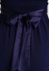 Abito navy con corpetto arricciato, dotato di una cintura in satin annodata a fiocco in vita. Tessuto liscio e stoffa fluente.