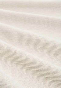 Baumwollstoff mit einer subtilen gerippten Textur in einer hellbeigen Farbe, die sanfte Falten und glatte Oberflächenmuster zeigt.