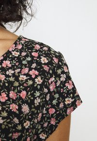 Blomstermønstret stof i sort, med pink og grønne blomster. Korte ærmer med v-hals og tekstureret materiale.