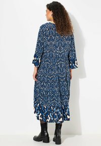 Blå mönstrad maxiklänning med trekvartsärmar, volangkant och abstrakta mönster i grädde och mörkblå nyanser. Svarta ankelboots.