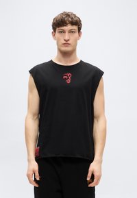 Μαύρο βαμβακερό αμάνικο μπλουζάκι με κόκκινο γραφικό σχέδιο στο στήθος και μια μικρή κόκκινη ετικέτα στο τελείωμα.