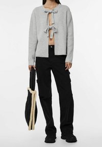 Cardigan grigio a coste con taglio, caratterizzato da due fiocchi sul davanti. Abbinato a pantaloni cargo neri e una borsa trapuntata nera con rifiniture crema.