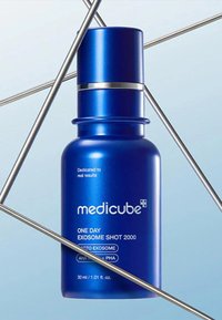 Blå sprayflaska med metallicfinish, silverdetaljer och vit text. Etiketter inkluderar "Medicube" och "One Day Exosome Shot 2000."
