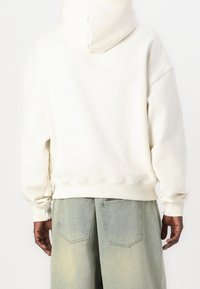 Felpa crema con vestibilità rilassata, polsini e orlo a costine. Abbinata a jeans baggy blu chiaro con tasche a toppa sul retro.