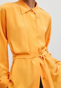 Langärmliges Hemd in leuchtendem Orange, aus glattem Stoff. Verfügt über einen klassischen Kragen, eine Knopfverschluss und eine gebundene Taillenverzierung.