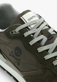 Sportlich gestalteter Schuh in olivgrün mit grauen Wildlederelementen; verfügt über ein Totenkopf- und gekreuzte Knochen-Logo, graue Schnürsenkel und eine weiße Zwischensohle.