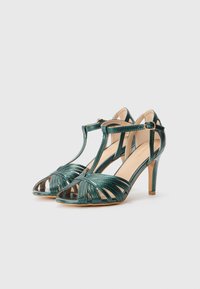 Teal metallic high-heeled sandals with an open toe, featuring strap detailing and a T-strap design, set on a slender, tapered heel.
