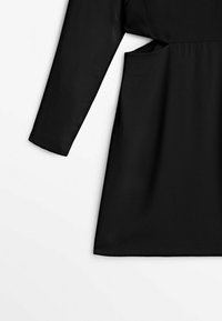 Svart klänning med långa ärmar, avslappnad passform och sidofickor. Tillverkad av ett slätt tyg med en enkel, odekorerad design.