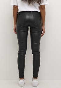 Musta tekonahka legginsit, joissa on korkea vyötärö, takataskut ja slim fit -malli, yhdistettynä valkoisiin lenkkareihin.