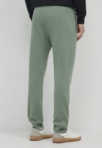 Hellgrüne Sweatpants mit elastischem Bund und Bündchen, ausgestattet mit Seitentaschen. Kombiniert mit weißen und grauen Sneakern.