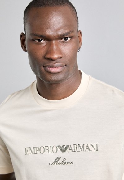 Beige Baumwoll-T-Shirt mit gesticktem "EMPORIO ARMANI Milano"-Logo in Dunkelgrün, Rundhalsausschnitt und kurzen Ärmeln.