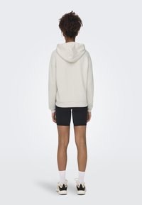 Light grey hooded sweatshirt with ribbed cuffs and hem, paired with black shorts. Model wears white crew socks and black sneakers.