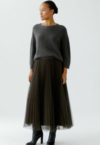 Gray, fuzzy knit sweater with a round neck paired with a long, pleated tulle skirt in dark green and black ankle boots.