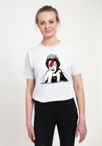 Bílý bavlněný tričko s grafickým designem korunované postavy se rozděleným obličejem, který obsahuje červené a modré akcenty.