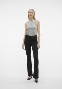 Haut sans manches gris clair, jean noir évasé et talons noirs. Design simple, tissu lisse, avec une silhouette ajustée et des détails subtils.