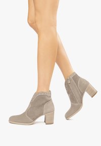 Grau samtige Knöchelstiefel mit einem durchbrochenen Design, Nietenakzenten und einem klobigen Absatz. Seitliche Reißverschlüsse für einfaches An- und Ausziehen.