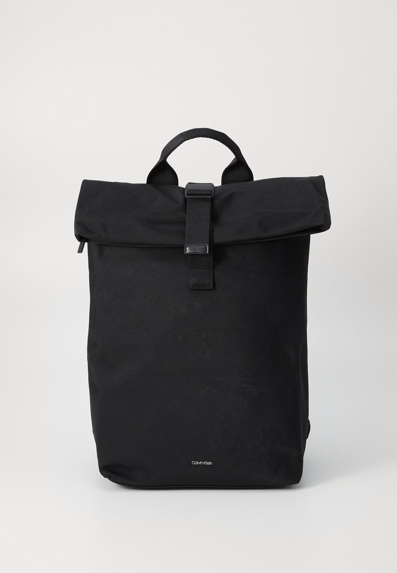 Sac à dos roulé noir en tissu texturé avec une sangle centrale et une fermeture à boucle. Présente un logo dans le coin inférieur avant.