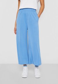 Pantalones de pierna ancha en azul claro con cintura elástica, dos bolsillos laterales y una textura suave, combinados con zapatillas blancas.