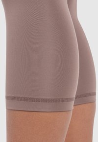 Pantaloni corti in tessuto taupe senza soluzione di continuità, con una superficie liscia e una vestibilità aderente, caratterizzati da un orlo decorativo cucito in fondo.