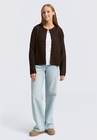 Brūns ribots kardigans ar pogām, valkāts pār baltu krekla, kombinēts ar gaiši ziliem platajiem džinsiem un bēšām platformas kurpēm.