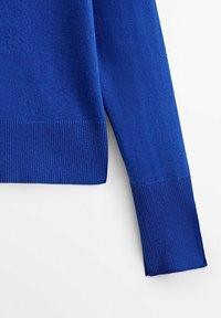 Niebieski sweter dzianinowy z ribbowym wykończeniem u dołu i przy mankietach. Gładka tekstura, lekko luźny krój oraz widoczne płaskie szwy wzdłuż krawędzi.