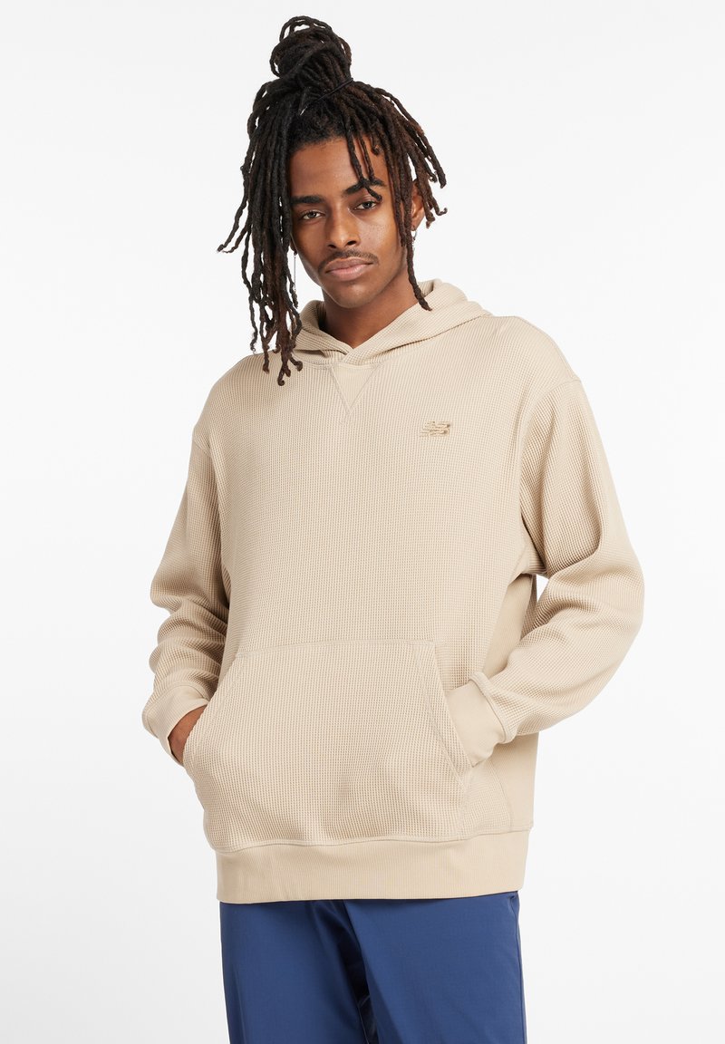 Beige hooded sweatshirt with a textured pattern, front pocket, and logo on the chest. The design features a relaxed fit with ribbed cuffs.