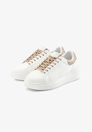 White low-top sneakers with beige laces and heel accents, textured sides, and thick white rubber soles on a white background.