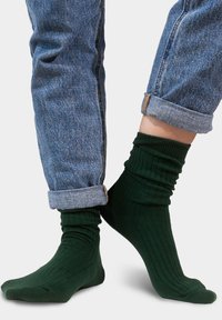 Zielone skarpetki w prążki, wykonane z miękkiego materiału, noszone z podwiniętymi niebieskimi dżinsami, podkreślające strukturę i dopasowany krój.