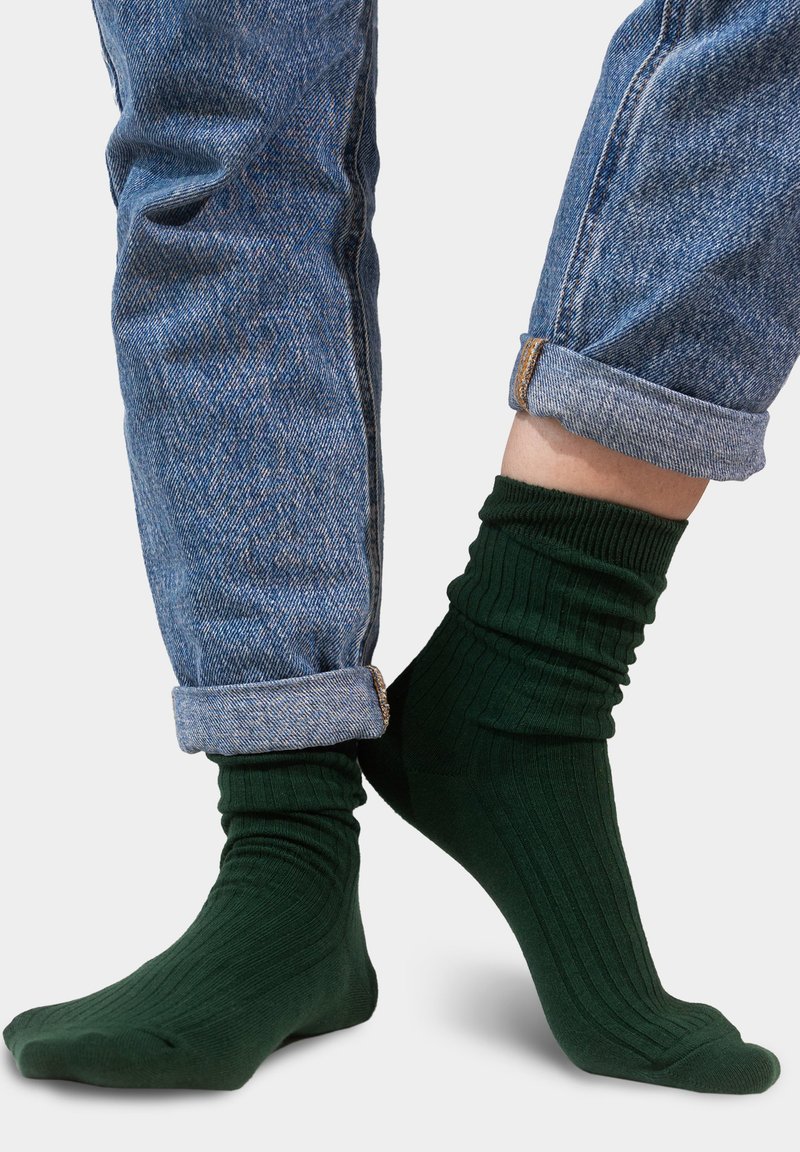 Zielone skarpetki w prążki, wykonane z miękkiego materiału, noszone z podwiniętymi niebieskimi dżinsami, podkreślające strukturę i dopasowany krój.
