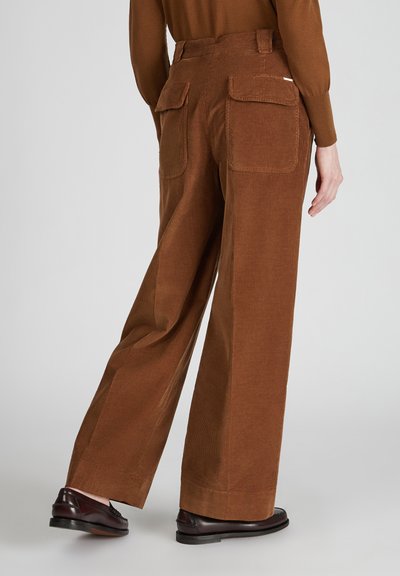 Bruine corduroy wijde broek met twee achterzakken en een subtiele textuur. Gecombineerd met donkere schoenen, gezien vanaf de achterkant.
