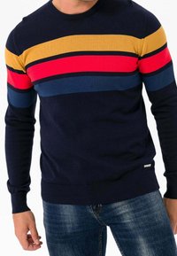 Pull bleu marine avec rayures horizontales multicolores en jaune, rouge, bleu foncé et bleu clair. Col et poignets côtelés, coupe ajustée.