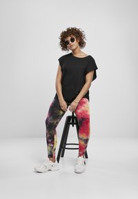 Svart kortermet topp kombinert med multikolorerte tie-dye leggings med rosa, gul og grønn mønster. Brukt med hvite treningssko.