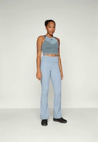 Blau gerippter Crop-Top mit rundem Ausschnitt und passenden hoch taillierten Schlaghosen. Schwarze Turnschuhe vervollständigen das Outfit.