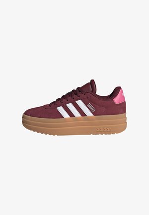 Burgundy suede sneaker with three white stripes, a pink heel accent, and a thick gum rubber sole. Features textured laces and branding.