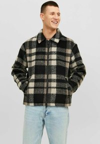 Giacca in pile a quadri neri e grigi con colletto, zip completa e tasche laterali. Presenta una texture morbida e un motivo geometrico.