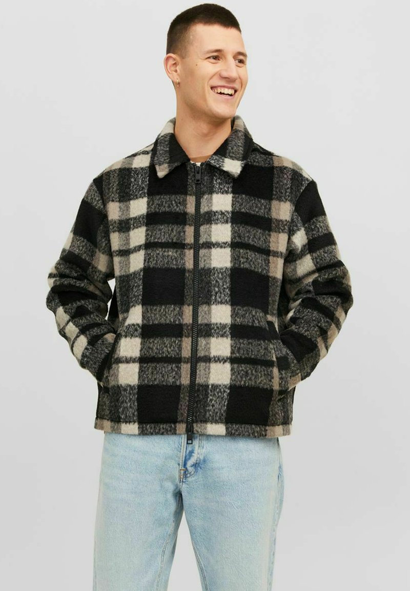 Giacca in pile a quadri neri e grigi con colletto, zip completa e tasche laterali. Presenta una texture morbida e un motivo geometrico.