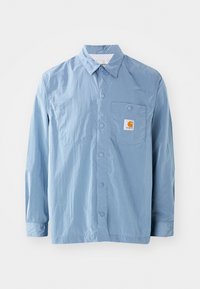 Chemise à boutons bleu clair en tissu léger, dotée d'une poche plaquée, de boutons-pression et d'une étiquette logo sur la poitrine.